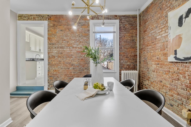 dining area featuring brick wall, radiator, a chandelier, and ornamental molding