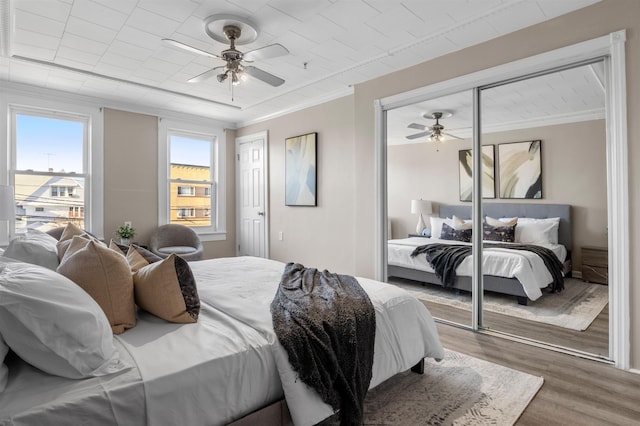 bedroom featuring ceiling fan, crown molding, wood-type flooring, and multiple windows