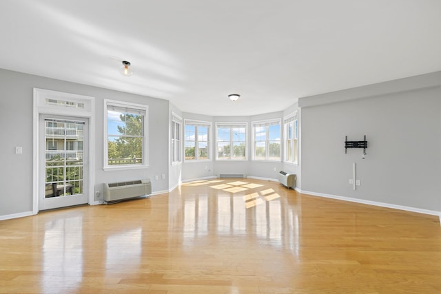 unfurnished living room with light hardwood / wood-style flooring, a baseboard heating unit, and a wall mounted air conditioner