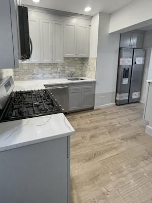 kitchen featuring gray cabinets, backsplash, stainless steel fridge, stove, and light wood-type flooring