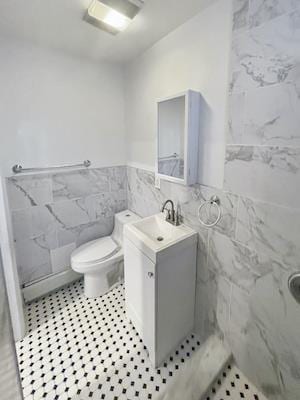 bathroom featuring tile walls, vanity, toilet, and walk in shower