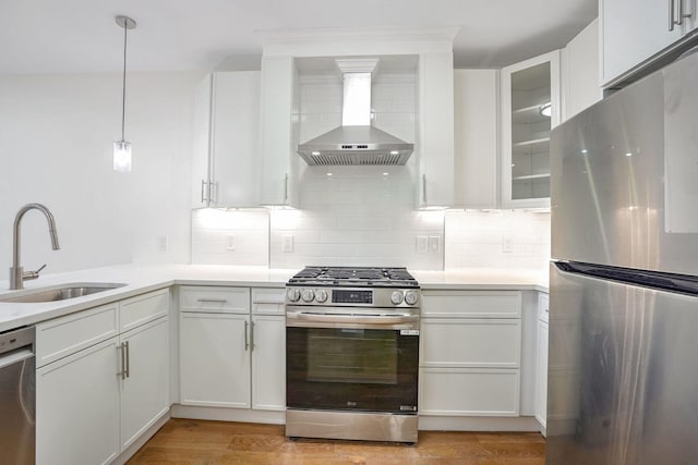 kitchen with light wood-type flooring, wall chimney exhaust hood, stainless steel appliances, sink, and white cabinets