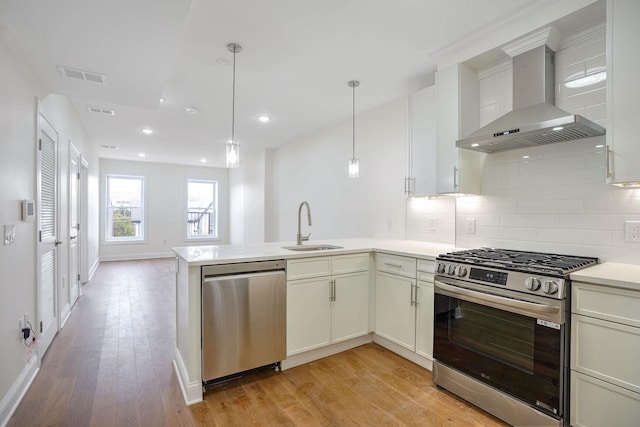 kitchen featuring sink, wall chimney exhaust hood, appliances with stainless steel finishes, decorative light fixtures, and light hardwood / wood-style floors