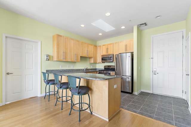 kitchen featuring visible vents, light brown cabinetry, appliances with stainless steel finishes, a skylight, and a peninsula