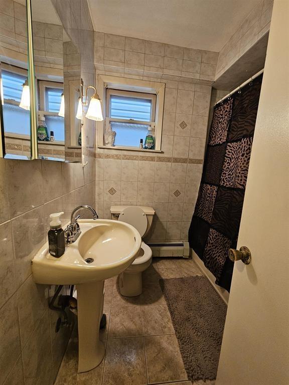 full bath with tile walls, curtained shower, tile patterned floors, a baseboard heating unit, and toilet