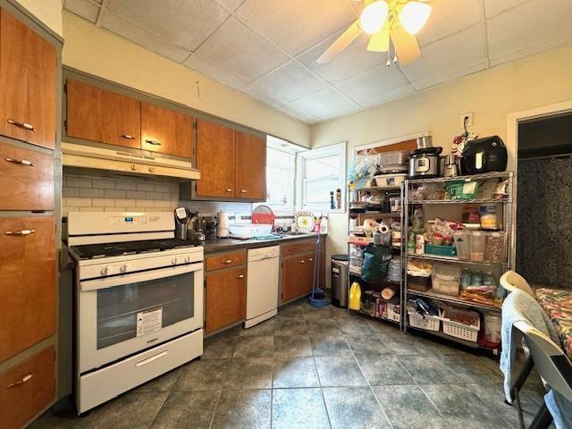 kitchen featuring ceiling fan, white appliances, brown cabinetry, decorative backsplash, and under cabinet range hood