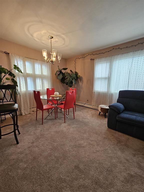 carpeted dining space featuring a baseboard heating unit, a notable chandelier, and plenty of natural light