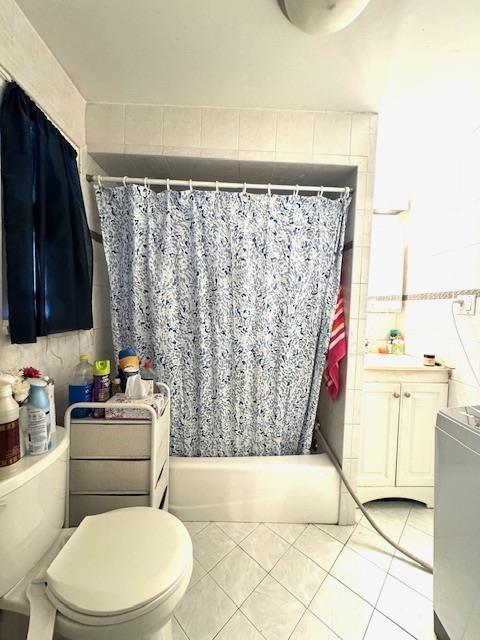 full bathroom with shower / tub combo with curtain, tile patterned floors, toilet, and tile walls