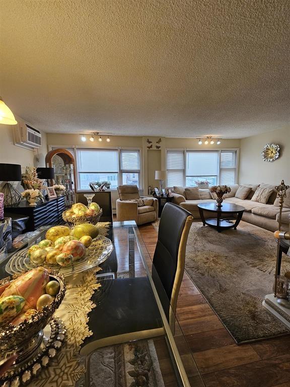 dining space featuring a textured ceiling, wood finished floors, rail lighting, and a wall mounted air conditioner
