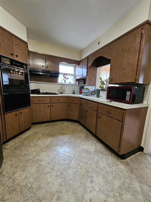kitchen with light countertops, black appliances, light tile patterned flooring, and under cabinet range hood