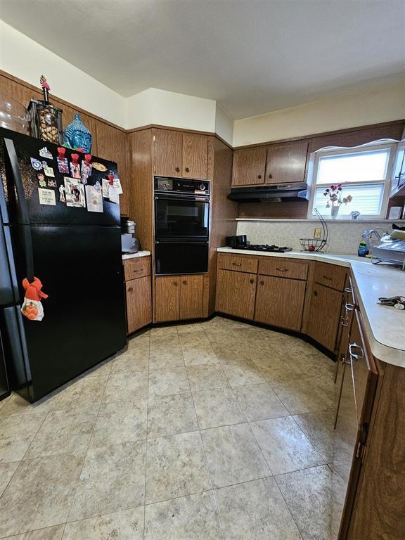 kitchen with brown cabinetry, light countertops, under cabinet range hood, and black appliances