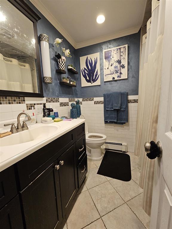 bathroom featuring baseboard heating, toilet, tile patterned floors, tile walls, and ornamental molding