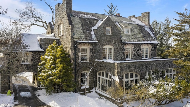 exterior space with a chimney, a high end roof, and stone siding