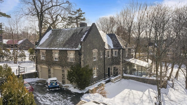 view of snow covered exterior with a garage, stone siding, a sunroom, and a chimney