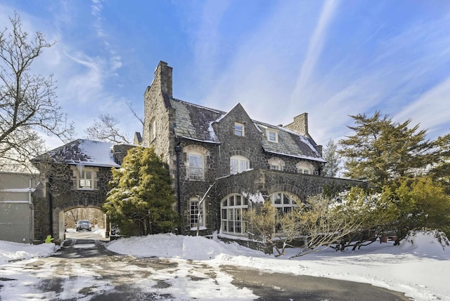 view of front facade featuring a high end roof, a chimney, and stone siding