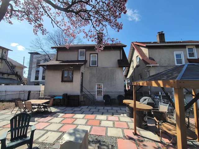 back of house featuring a chimney, fence, a patio, entry steps, and stucco siding