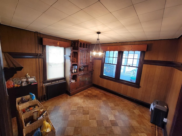 unfurnished dining area with wood walls, radiator, and a notable chandelier