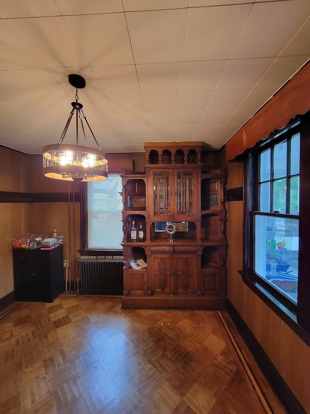 dining area featuring wood walls, radiator, and a notable chandelier