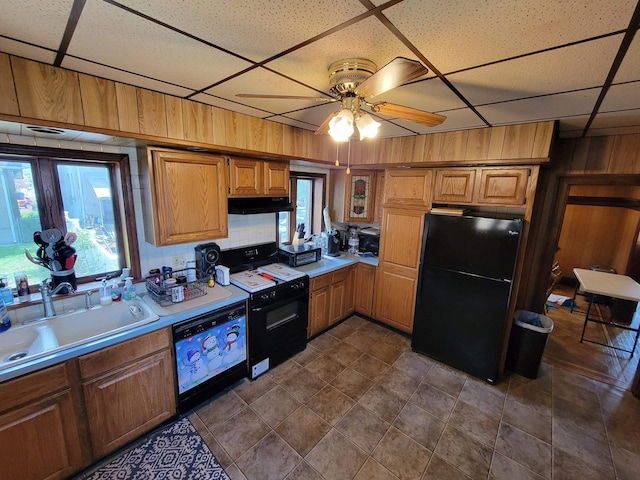kitchen with wood walls, light countertops, under cabinet range hood, a sink, and black appliances
