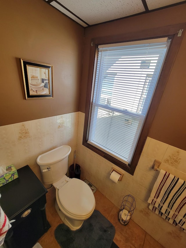 bathroom with tile walls, wainscoting, and toilet