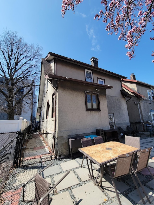 rear view of house with fence, outdoor dining area, stucco siding, a gate, and a patio area