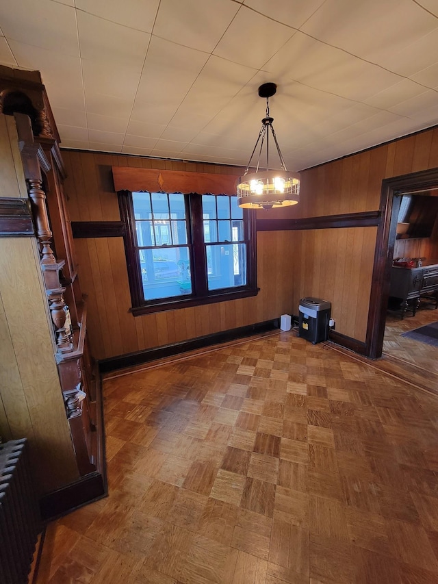 unfurnished dining area featuring wooden walls, an inviting chandelier, and radiator
