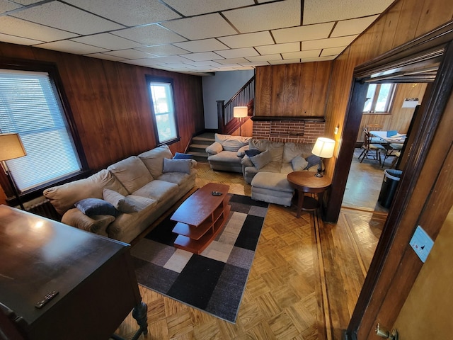 living area featuring plenty of natural light, wood walls, a paneled ceiling, and stairway