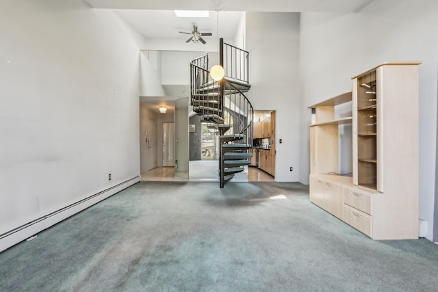unfurnished living room with ceiling fan, a high ceiling, baseboard heating, stairway, and carpet