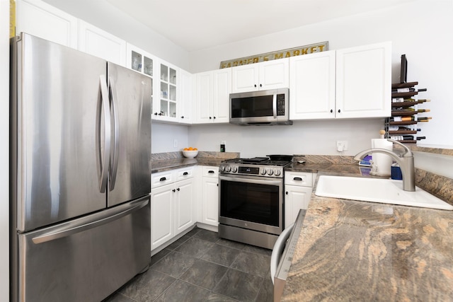 kitchen featuring appliances with stainless steel finishes, white cabinetry, dark stone counters, and sink