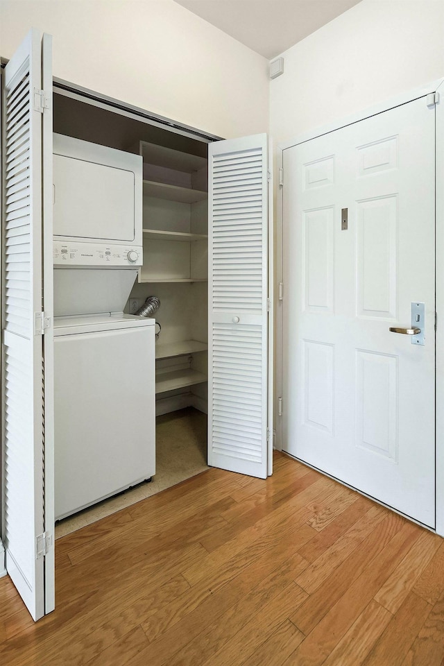 washroom with stacked washer and clothes dryer and hardwood / wood-style flooring