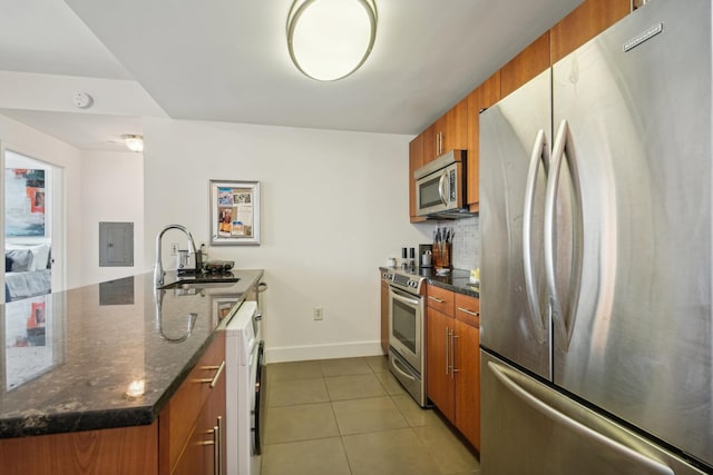 kitchen with dark stone countertops, sink, light tile patterned floors, and stainless steel appliances