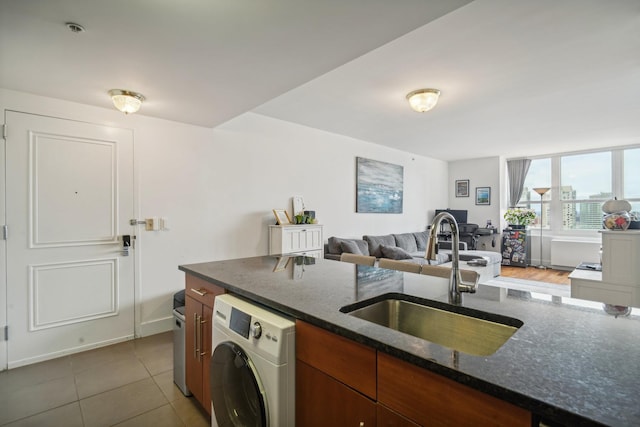 kitchen with sink, tile patterned flooring, dark stone counters, and washer / dryer