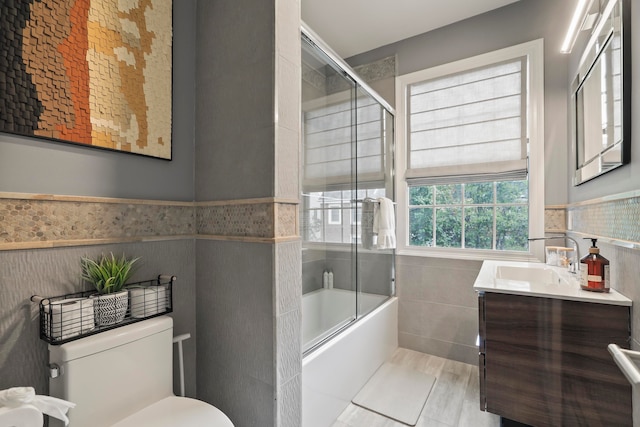 full bathroom with tile walls, enclosed tub / shower combo, tile patterned floors, vanity, and toilet