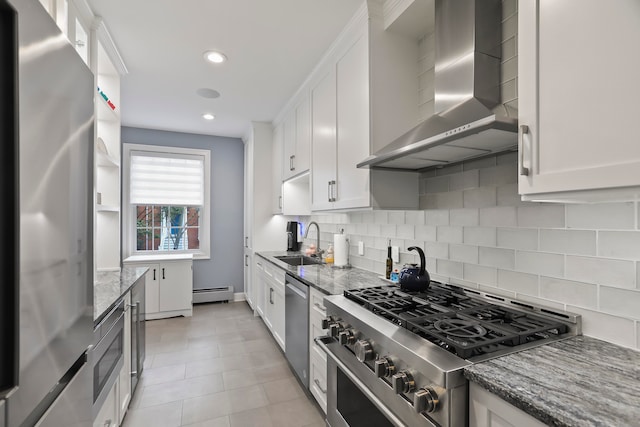 kitchen featuring wall chimney range hood, appliances with stainless steel finishes, a baseboard radiator, and white cabinets