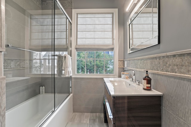 bathroom featuring tile walls, shower / bath combination with glass door, and vanity