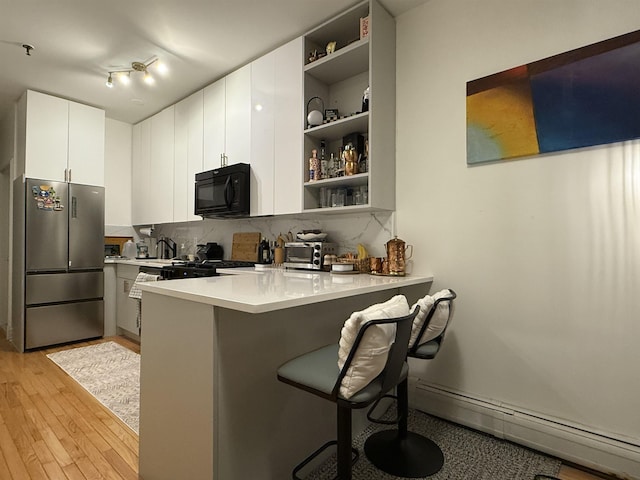 kitchen featuring black appliances, a kitchen breakfast bar, white cabinets, a baseboard radiator, and kitchen peninsula