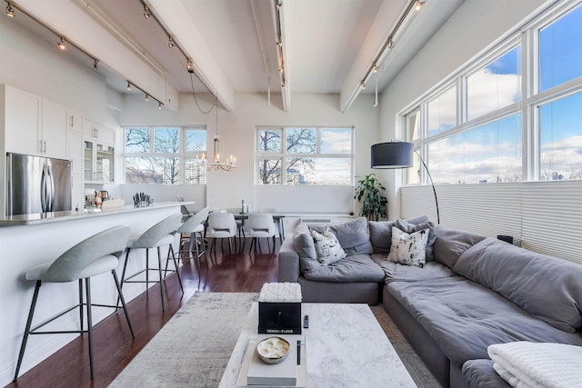 living room featuring beamed ceiling, rail lighting, dark wood-type flooring, and an inviting chandelier