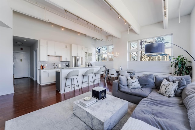 living room featuring sink, rail lighting, beam ceiling, dark hardwood / wood-style floors, and a notable chandelier