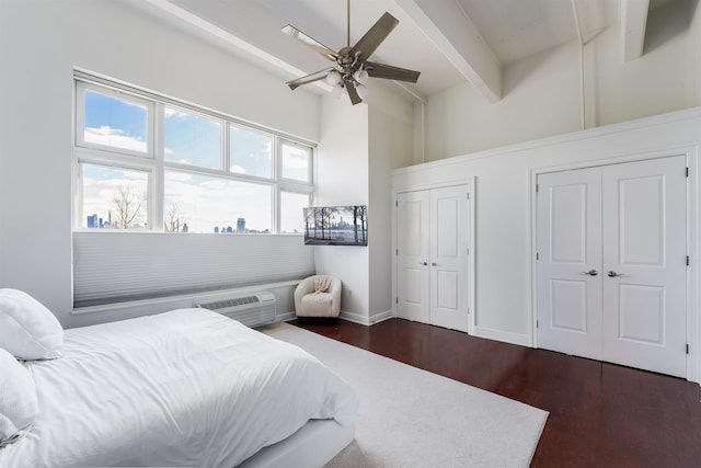 bedroom featuring two closets, a wall mounted air conditioner, ceiling fan, dark wood-type flooring, and beam ceiling