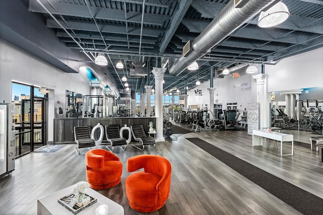 gym with ornate columns, a high ceiling, and wood finished floors