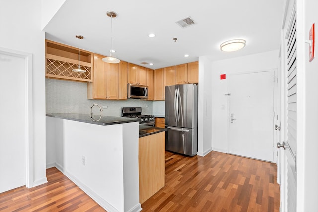 kitchen with a peninsula, wood finished floors, dark countertops, appliances with stainless steel finishes, and backsplash