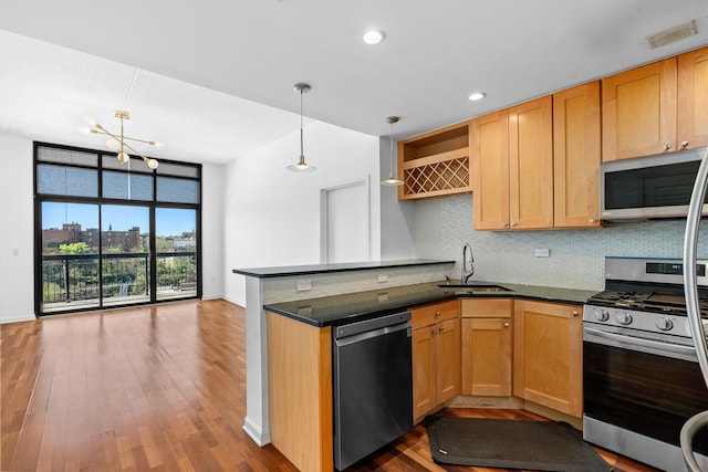 kitchen featuring dark countertops, a sink, stainless steel appliances, a peninsula, and decorative backsplash
