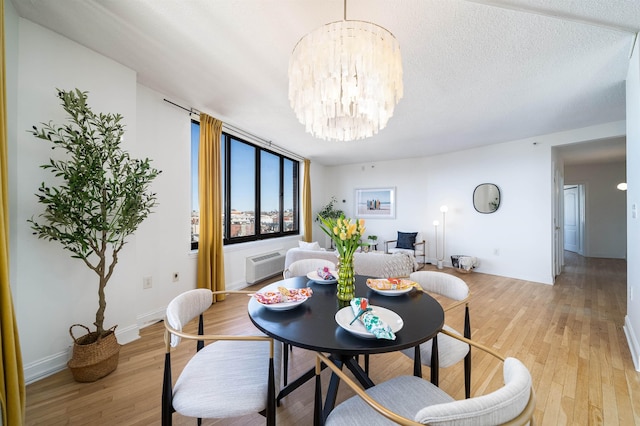 dining room with a textured ceiling, a wall unit AC, baseboards, light wood-type flooring, and an inviting chandelier