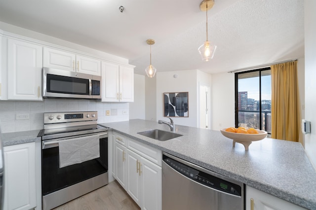 kitchen with a sink, white cabinetry, appliances with stainless steel finishes, decorative backsplash, and decorative light fixtures