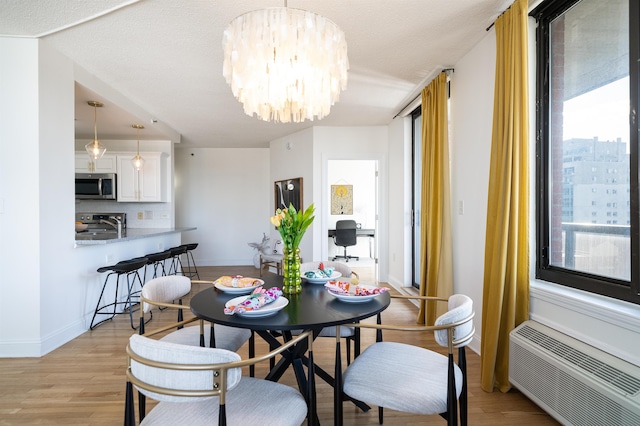 dining space featuring a chandelier, light wood finished floors, a wall mounted AC, and plenty of natural light