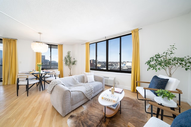 living room featuring a wall unit AC, a notable chandelier, baseboards, light wood-style floors, and a view of city