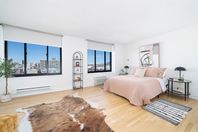 bedroom featuring multiple windows, baseboard heating, wood finished floors, and a city view