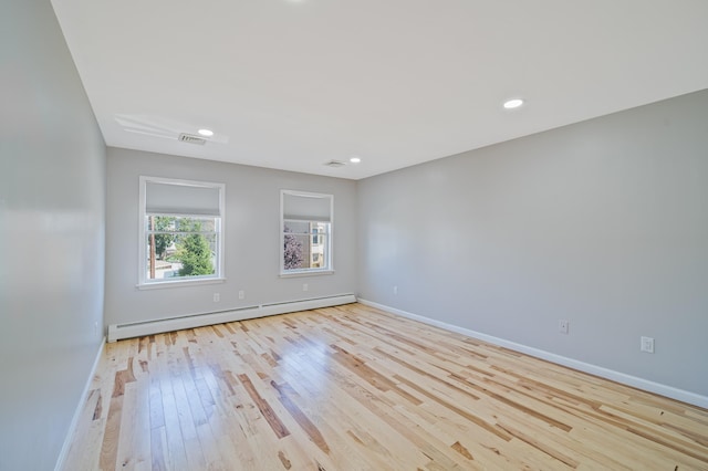 empty room featuring a baseboard radiator, visible vents, baseboards, and wood finished floors