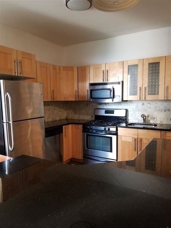 kitchen with sink, light brown cabinets, dark stone counters, stainless steel appliances, and backsplash