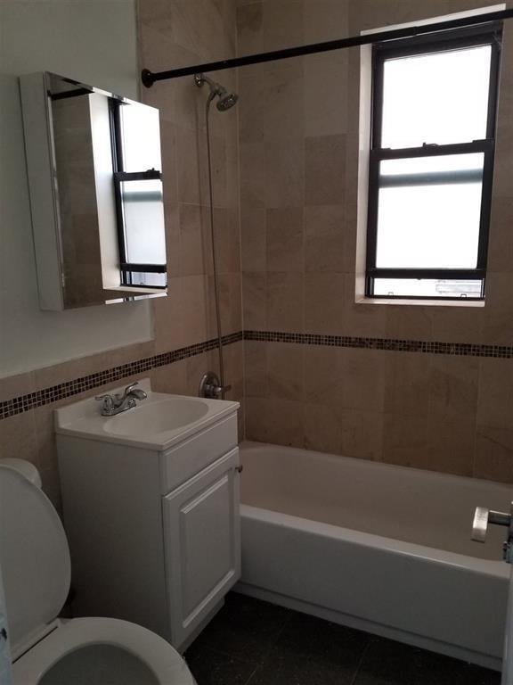 full bathroom featuring tile patterned flooring, tile walls, vanity, toilet, and tiled shower / bath